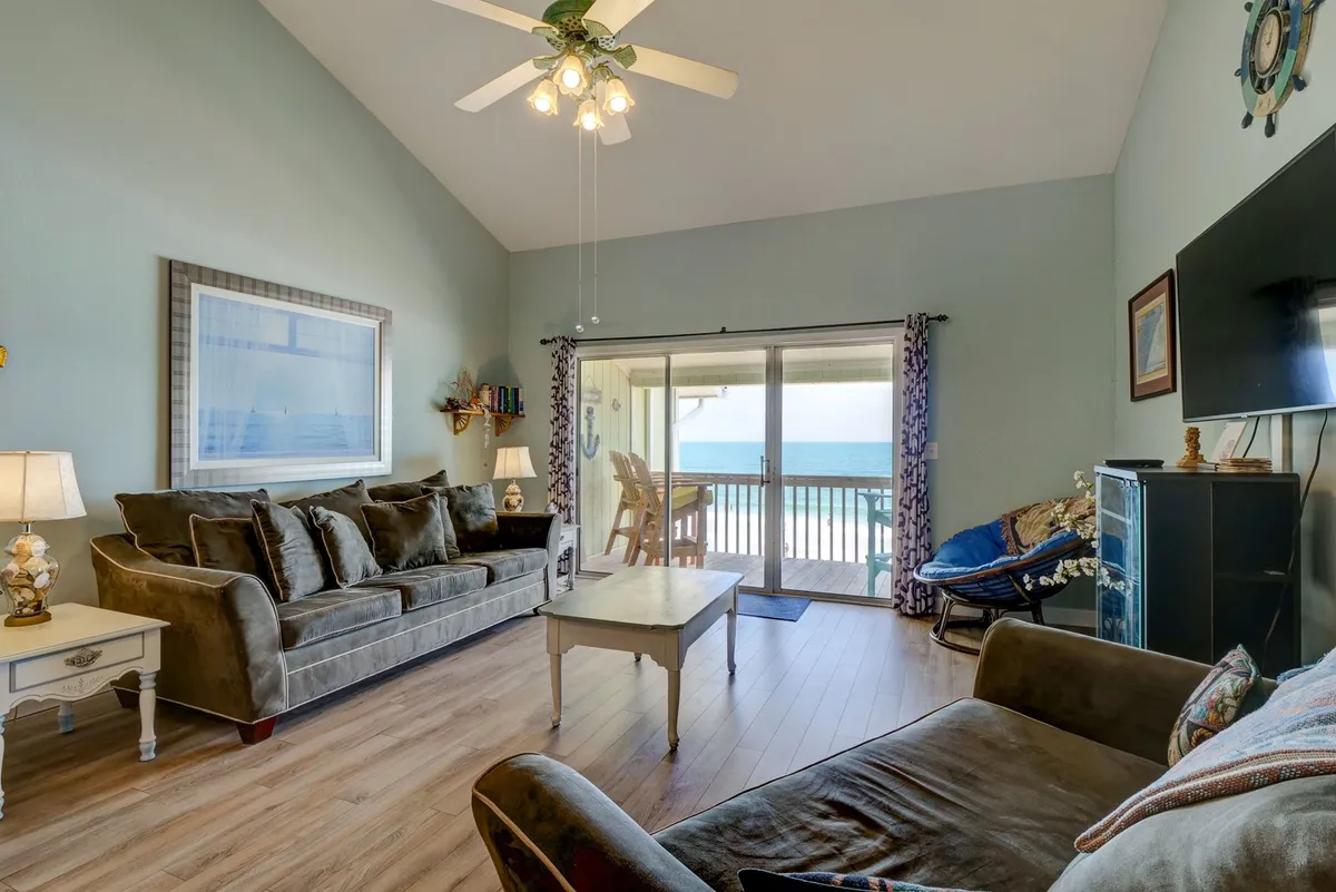 A welcoming living area with a sofa and coffee table facing sliding glass doors that open to an expansive ocean view. The space is filled with natural light, blending comfort with the allure of the nearby beach.
