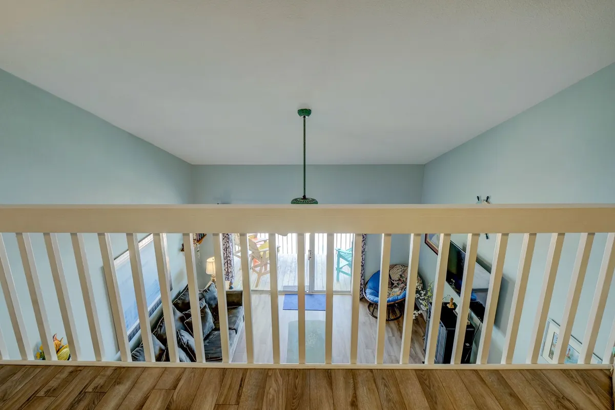 A cozy living space extending to a balcony with colorful outdoor chairs. The image captures sunshine streaming in, a comfortable sofa, and the welcoming transition from interior to the private covered deck.