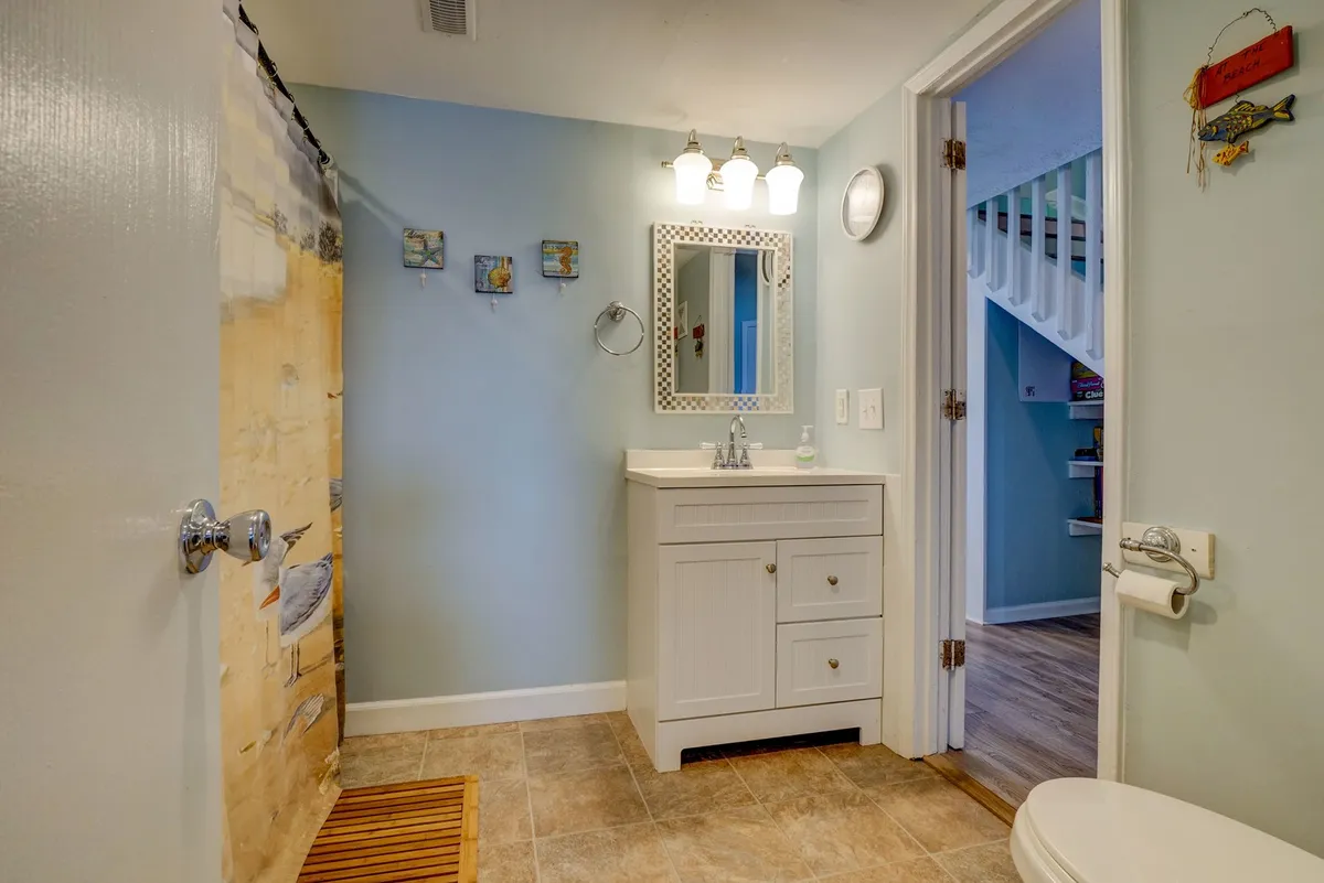 A modern, refreshing bathroom featuring a vanity with sink, mirror, shower curtain, and wall art. The clean design suggests both functionality and comfort, ideal for morning routines or winding down after a day at the beach.