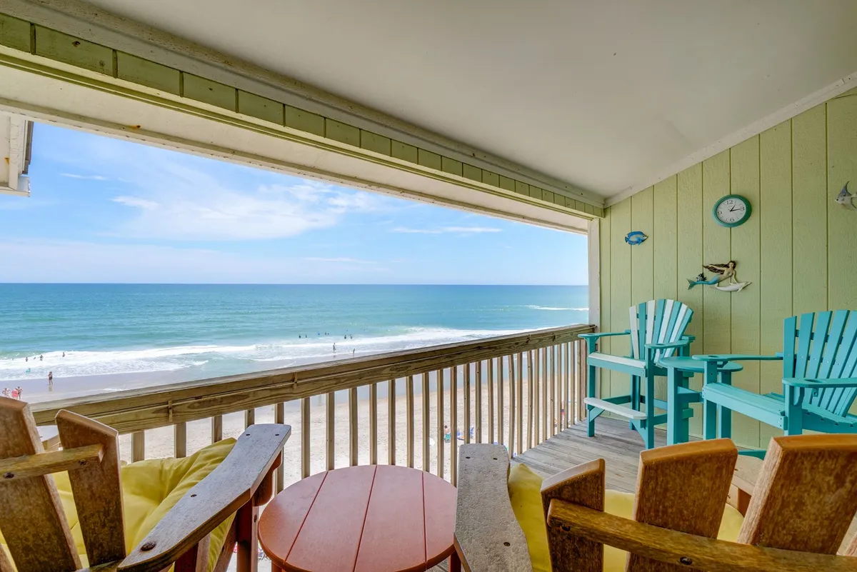 An inviting exterior balcony scene with colorful chairs and a small table, overlooking the peaceful beach and ocean horizon. The setting is perfect for sipping coffee, sharing a quiet conversation, or unwinding while watching the sunset together.