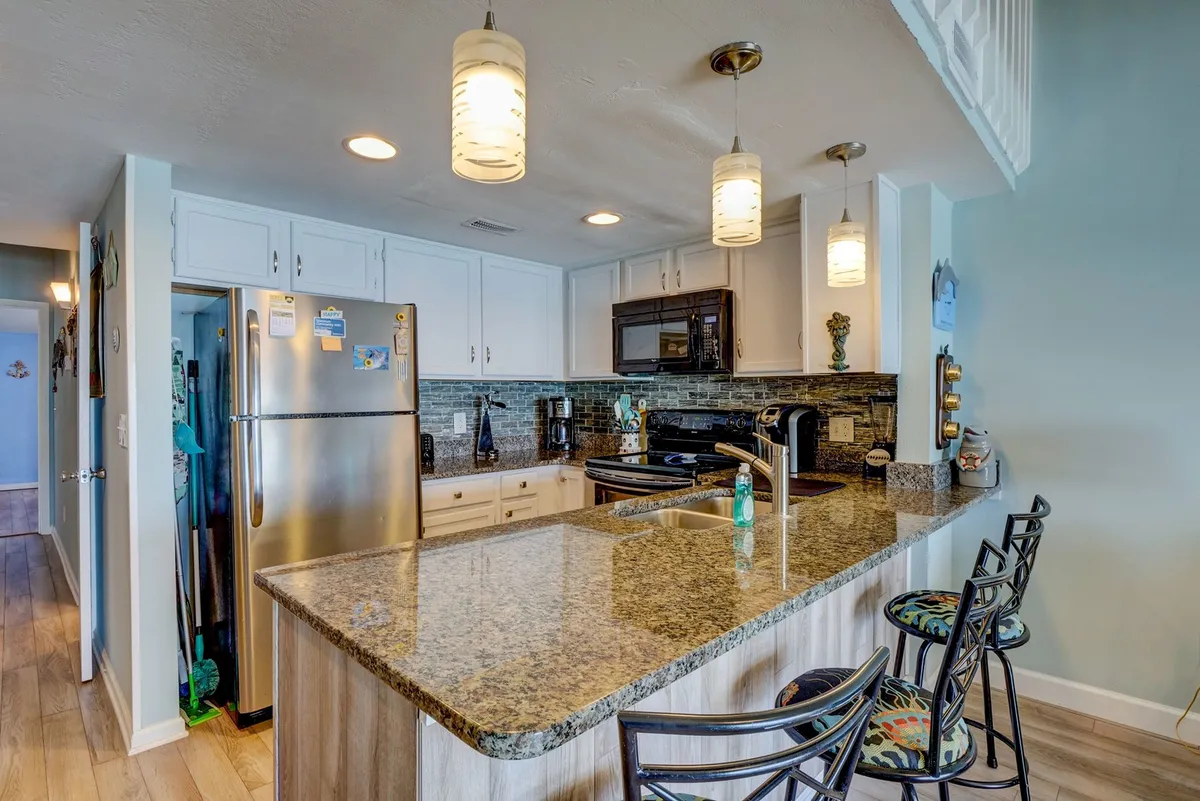 A modern kitchen with striking granite countertops, stainless steel appliances, bar stools, and pendant lighting. The countertop and bar area are clearly highlighted for informal dining or gathering.