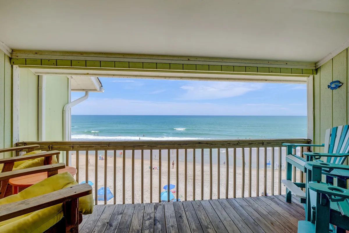 A private balcony or deck furnished with comfortable chairs faces the ocean. The view is expansive, showcasing the sandy beach and the sparkling waters beyond. This tranquil spot is ideal for enjoying snacks, downtime, or soaking in the ocean breeze after a day of activities.